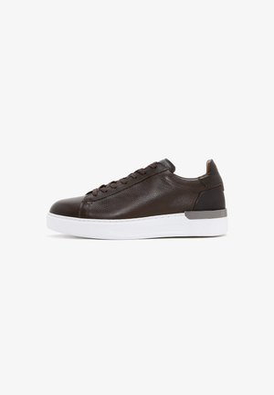 Zapatilla baja de cuero marrón oscuro con superficie texturizada, cordones marrones a juego y suela blanca gruesa con acento gris en el talón.