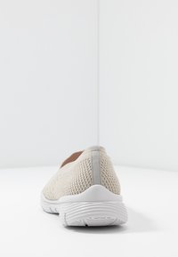 Zapato ligero color beige tipo slip-on, hecho de una malla transpirable, con parte superior texturizada y suela de goma blanca; cuenta con sutiles acentos grises.