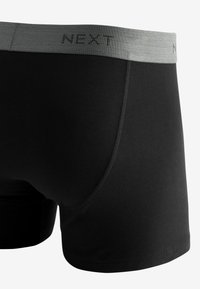 Boxer shorts noirs avec une ceinture élastique grise arborant le logo "NEXT". Texture lisse avec un design ajusté et des détails de couture contrastants.
