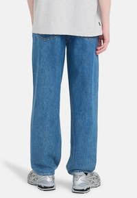 Jeans de mezclilla azul holgados con un acabado texturizado, que presentan un diseño de pierna recta y bolsillos traseros, combinados con zapatillas plateadas.