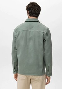 Kurze grüne Jacke aus robustem Stoff. Verfügt über einen Kragen, knöpfbare Manschetten und eine yoke über dem Rücken. Glatte Textur und lockere Passform.