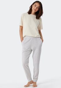 T-shirt a maniche corte di colore crema chiaro abbinato a pantaloni da jogging grigi. I pantaloni hanno una vita elasticizzata e polsini affusolati, offrendo una vestibilità comoda.