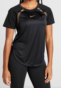 Camiseta deportiva negra de Nike de manga corta, con detalles de malla, dobladillo curvado y logo dorado en el pecho. Tejido ligero.