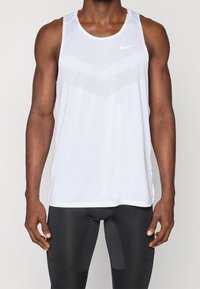 Valkoinen Nike-hihaton paita, jossa on teksturoidusta chevron-muotoilusta tehty kuvio edessä. Kevyt kangas, ilman hihoja, ja pyöreä pääntie.