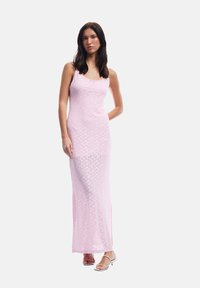 Robe maxi rose avec un corsage ajusté, texture en dentelle et fentes sur les côtés. Associée à des sandales minimalistes ; détail à col côtelé.