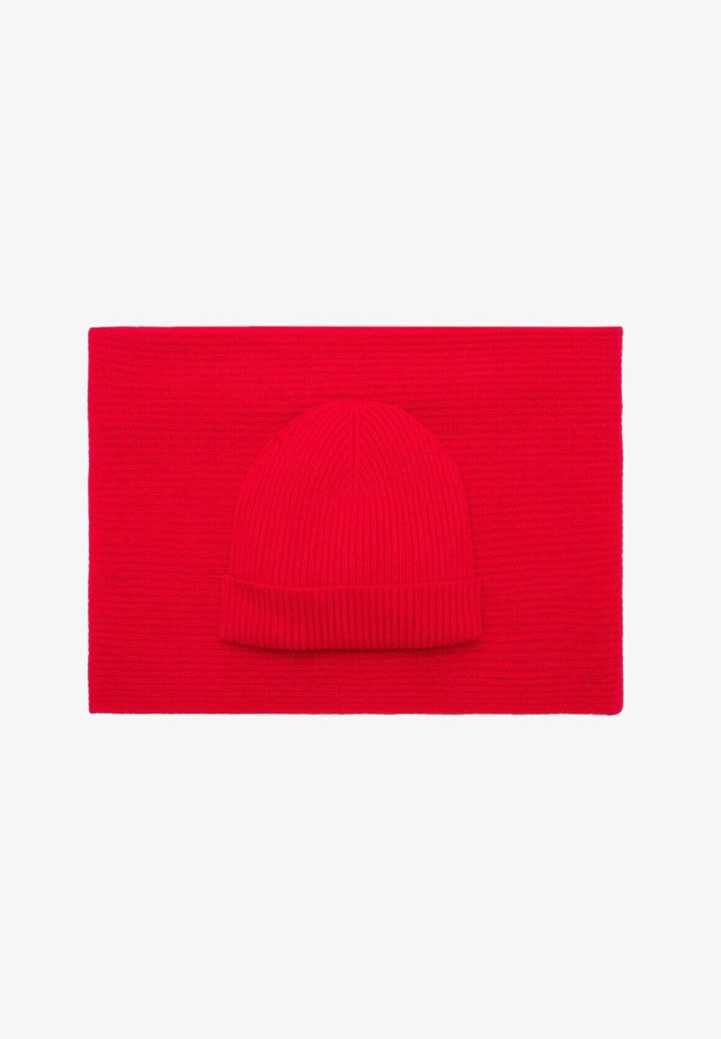 Berretto di lana rosso a maglia sopra una sciarpa piatta coordinata. Entrambi i pezzi presentano una texture a coste e sono di un uniforme colore rosso brillante.