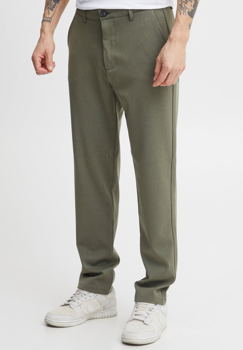 Olive green tailored trousers with a smooth texture, featuring a button closure, side pockets, and a straight leg design, paired with white sneakers.