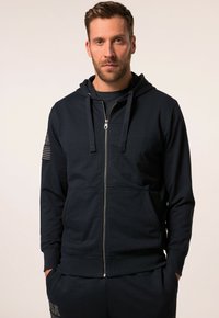 Navy zip-up hoodie in soft fabric, featuring a kangaroo pocket, drawstring hood, and a flag patch on the left arm.