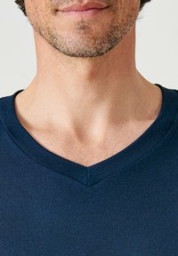 T-shirt navy blu con scollo a v realizzato in tessuto a costine, caratterizzato da una superficie liscia e un design aderente, visto dalla gola in su.