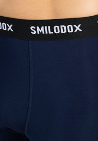 Marina sportkalsonger med svart elastisk midja och vit "SMILODOX" text. Slät textur, åtsittande design och minimal sömnadsdetalj.