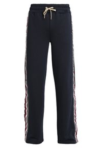 Námořnické tepláky s elastickým pasem a šňůrkou, se zvlněnými červenými a bílými pruhy po stranách. Měkká textilní struktura.