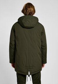 Oliwkowa parka z kapturem o długości do połowy uda, z regulowanym pasem, teksturowanym materiałem i prostym krojem oraz minimalną ilością dodatków.