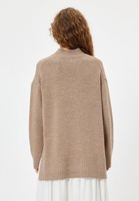 Maglione beige lavorato a maglia con colletto alto, vestibilità leggermente over-sized, orlo a coste e maniche lunghe. Texture liscia con una silhouette più ampia.