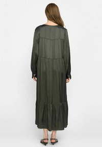 Robe longue couleur vert olive en tissu satiné, à manches longues, avec une taille froncée et une jupe évasée à ourlet superposé.