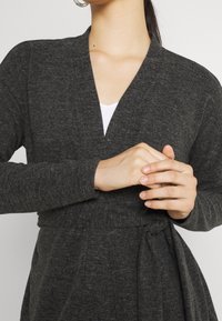 Grå kappa med mjuk textur, långa ärmar, djup V-ringning och ett tygband i midjan, som visar en avslappnad design.