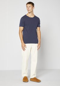 Námořnické tričko s kulatým výstřihem, krátké rukávy, spárované se světle béžovými kalhotami a hnědými semišovými slip-on botami. Jednoduchý design, čisté linie a neutrální barvy.