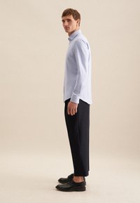 Camicia button-up azzurro chiaro con maniche lunghe, abbinata a pantaloni scuri a sigaretta e scarpe nere. La camicia presenta un colletto classico e una texture sottile.