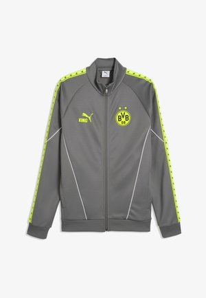 Graue Sportjacke mit Reißverschluss mit gelbem Puma-Logo, Text "KING" und BVB 09 Fußballvereinswappen, mit gelben Streifen an den Ärmeln.