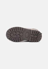 Semelle de botte marron avec des profondeurs caractéristiques et des motifs croisés, présentée sur un fond blanc uni.