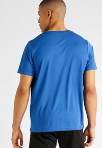 Blauw sportshirt met korte mouwen van gladde stof, met een ronde hals en een relaxte pasvorm, gedragen met zwarte shorts.