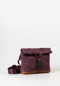 Bordeauxfarbene Rolltop-Tasche mit braunem Lederboden, verstellbarem Schultergurt und schwarzem Kunststoffverschluss. Auf der Vorderseite mit geprägtem Logo.