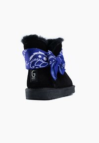 Botín de ante negro con un lazo de bandana azul. Presenta un forro interior suave y una suela de goma texturizada para mayor agarre. Logo de la marca visible.