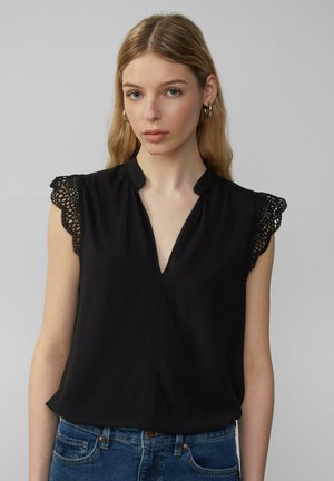Sort bluse med v-hals og korte ærmer med blondekant. Stoffet har en glat tekstur og bæres sammen med blå denimjeans.