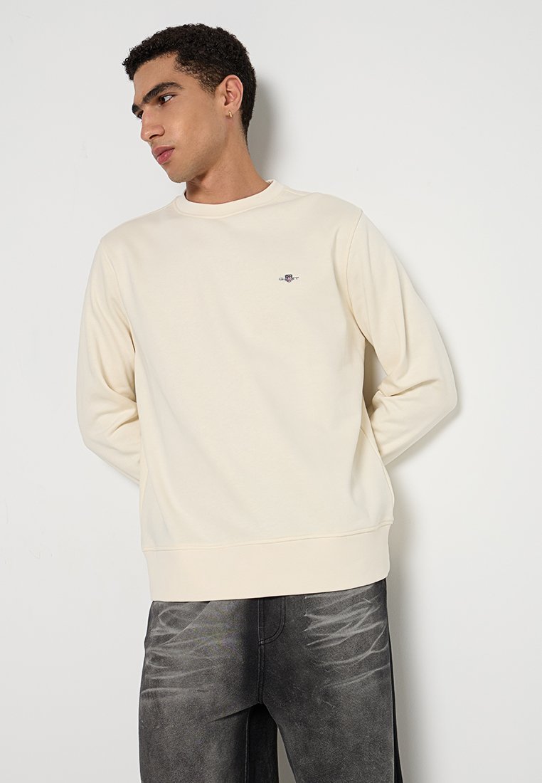 Helle beige Sweatshirt mit Rundhals, langen Ärmeln und Rippbündchen. Verfügt über ein kleines gesticktes Logo auf der Brust. Glatte Textur.