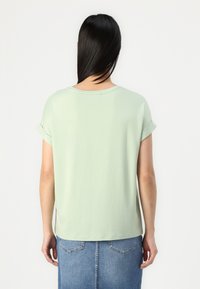 Hellgrünes T-Shirt mit kurzen Ärmeln und rundem Halsausschnitt. Weicher Stoff, lockere Passform, leicht umgeschlagene Bündchen. Kombiniert mit einem Jeansrock.