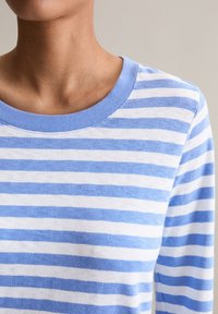 Sweter w paski z naprzemiennymi jasnoniebieskimi i białymi paskami, z okrągłym żebrowanym dekoltem i miękką fakturą. Skupienie na górnej części ciała.