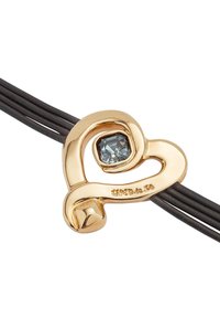 Colgante en forma de corazón bañado en oro con una piedra preciosa azul, unido a tres cuerdas de cuero negro. Presenta una superficie lisa y un diseño escultórico.