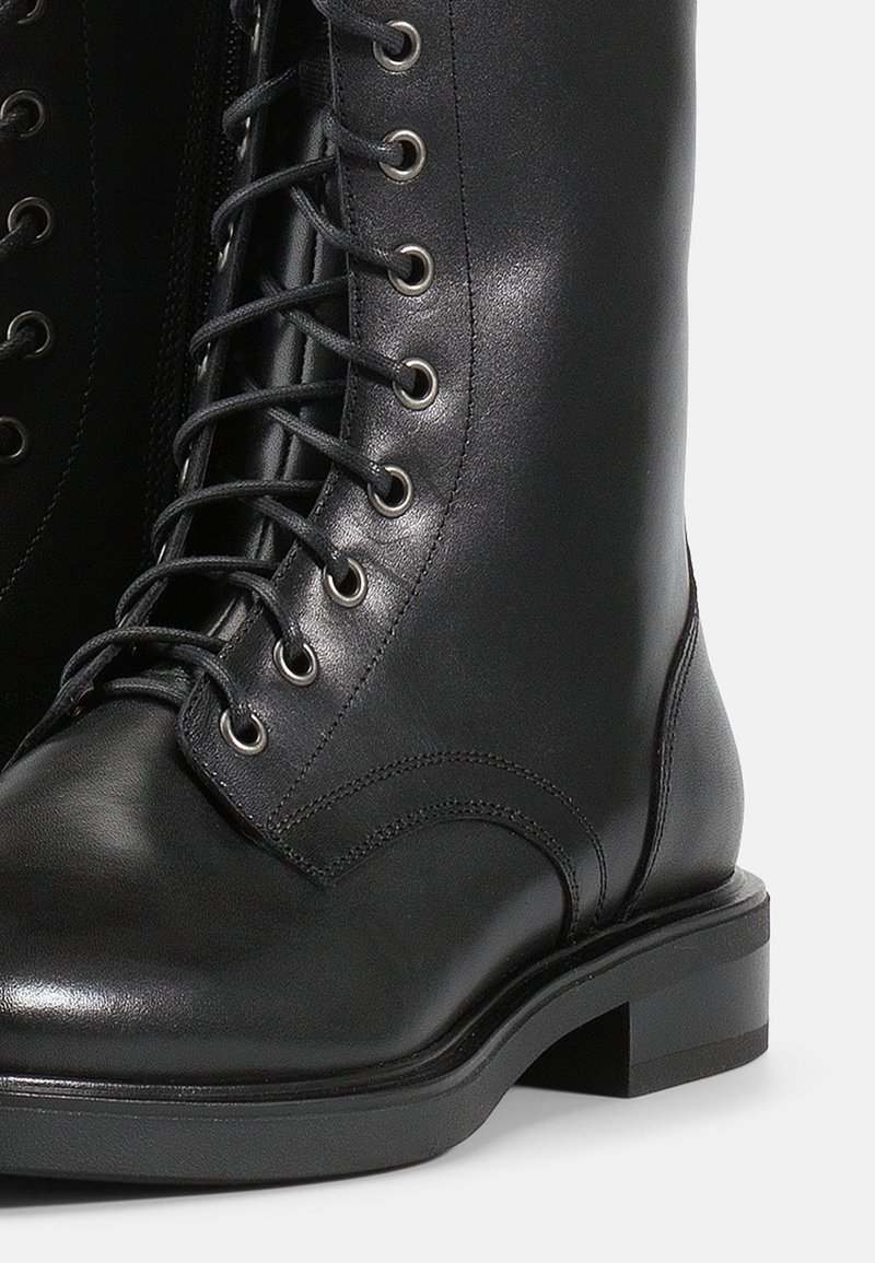 Schwarze Leder Schnürstiefel mit Metallösen, runder Spitze, robuster Sohle, glatter Textur und seitlichem Reißverschlussdetail für einfaches Anziehen.