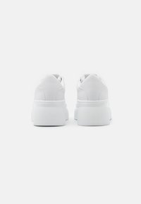 Baskets blanches avec une finition en cuir lisse, talons arrondis et semelles en caoutchouc texturé. Design minimaliste, sans logos ni motifs visibles.