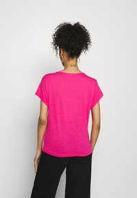 Camiseta corta de manga corta en un brillante color rosa, con un corte relajado, cuello redondo y tejido texturizado, combinada con pantalones negros sueltos.