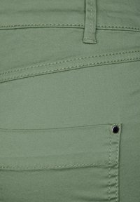 Vihreät kangashousut, joissa on sileä tekstuuri, näkyvät saumat ja pieni takatasku, jossa on musta metallipainike.