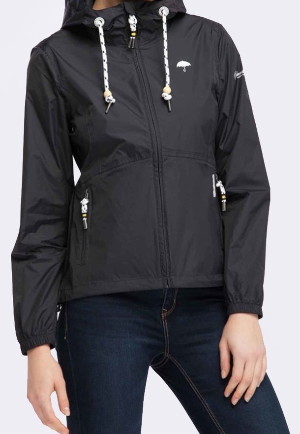 Giacca a vento nera con cappuccio, dotata di lacci bianchi e tasche con zip, indossata su jeans blu scuro.