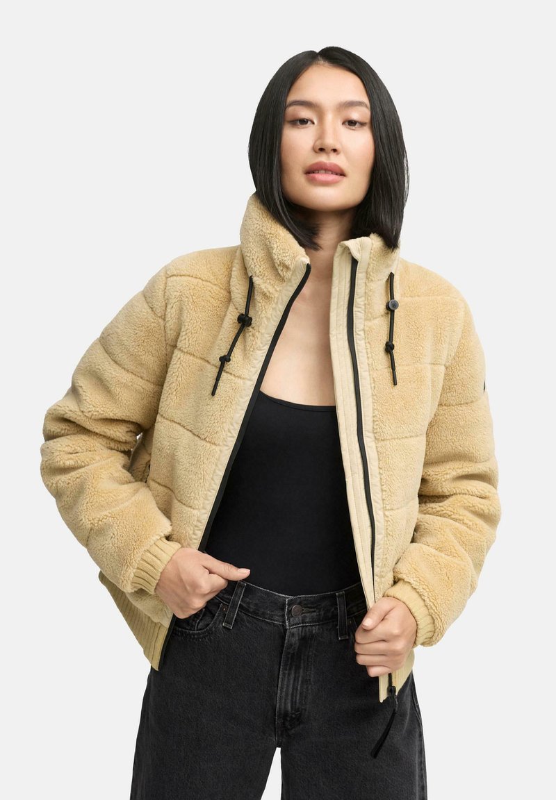 Beige Fleece-Jacke mit Reißverschluss, Stehkragen und schwarzen Kordelzügen. Verfügt über ein gestepptes Design und gerippte Bündchen.