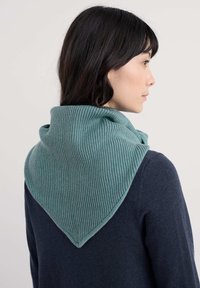 Trekantet, ribbestrikket halstørklæde i blødt, blågrønt stof, båret om halsen og supplerer en mørkeblå sweater.