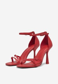 Sandali alti rossi con tacco, in morbida pelle, caratterizzati da fasce fini e una cintura alla caviglia regolabile, sorretti da un sottile tacco a stiletto.