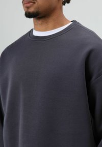 Donkergrijze trui met ronde hals, gemaakt van zachte stof. Voorzien van verlaagde schouders en een gladde textuur zonder patronen of prints.