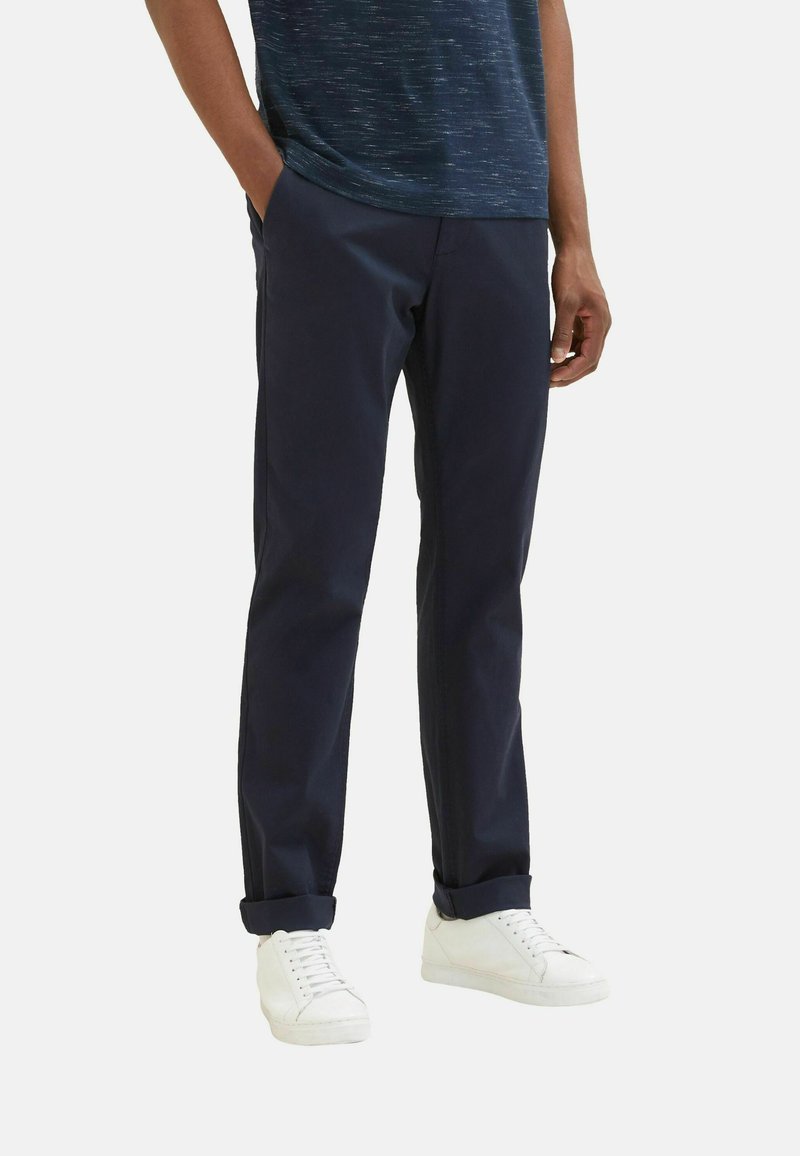 Navy chinos med rak passform, med sidofickor och uppvikta fållar, i kombination med vita sneakers. Tyget verkar slätt och hållbart.