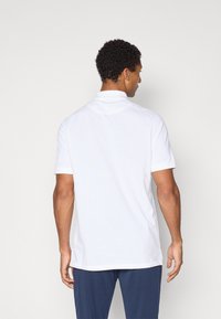 Hvid kortærmet polo-shirt med standart krave, glat stof og lige kant. Bæres med marineblå bukser.