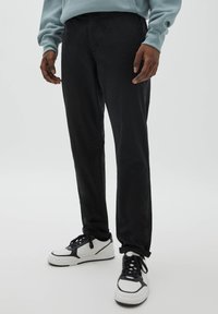 Černé kalhoty se zúženými nohavicemi z bavlněné směsi, s bočními kapsami, hladkou texturou a kontrastními bílými teniskami s černými detaily.