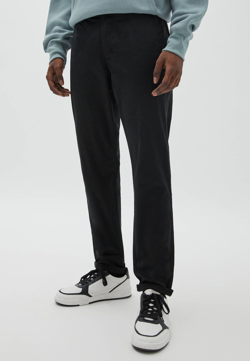 Černé kalhoty se zúženými nohavicemi z bavlněné směsi, s bočními kapsami, hladkou texturou a kontrastními bílými teniskami s černými detaily.