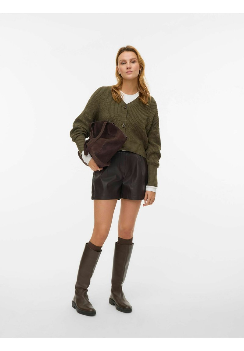 Cardigan verde oliva lavorato a maglia con bottoni, abbinato a pantaloncini in pelle neri. Stivali marroni alti fino al ginocchio e una borsa marrone scuro completano il completo.