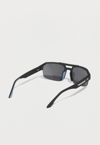 Lunettes de soleil rectangulaires noires avec des verres teintés foncés et des accents bleus sur les branches, vues de dos sur un fond blanc.