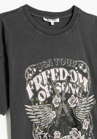 Grafisk mørkegrå t-shirt med "Freedom of Song" design, der viser to guitarer, roser og vinger. Blødt bomuldsstof, rund hals.