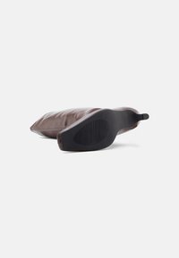 Καφέ μπότες με λεία υφή και μαύρη λαστιχένια σόλα. Διαθέτουν καμπυλωτό σχεδιασμό και διακριτικό πρότυπο πέλματος στη σόλα για καλύτερη πρόσφυση.