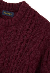 Maglione color bordeaux a maglia lavorata a trecce con scollo rotondo e dettagli a costine. Il tessuto appare spesso e testurizzato con motivi pronunciati.