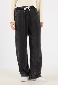 Zwarte, losvallende sweatpants met een gestructureerde afwerking, elastische tailleband en witte koord. Zijzakken en zichtbare stikseldetails.